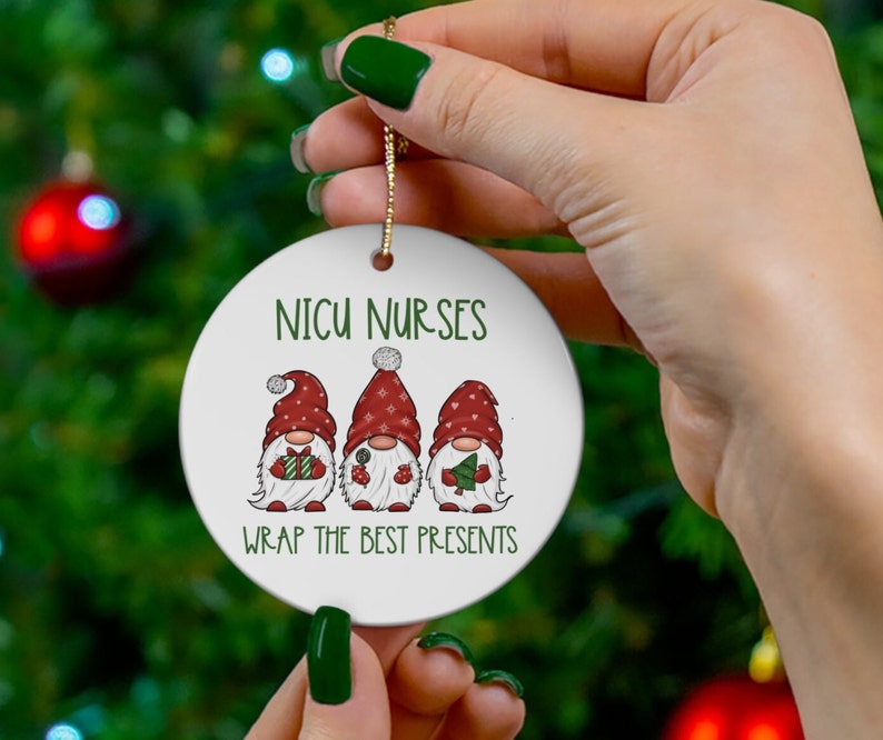 May include: White ceramic Christmas ornament with three gnomes wearing red hats and holding gifts. The ornament reads "NICU NURSES WRAP THE BEST PRESENTS".
