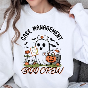 May include: White sweatshirt with a Halloween-themed graphic. The design features a ghost wearing a nurse's cap, holding a clipboard and a pumpkin basket. The text reads "CASE MANAGEMENT" and "BOO CREW".