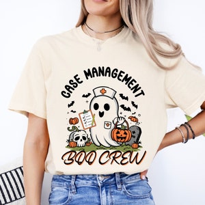 May include: A cream colored t-shirt with the text "Case Management Boo Crew" in black. A cartoon ghost wearing a nurse's hat and holding a clipboard and a pumpkin is in the center of the shirt.