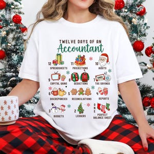 May include: White t-shirt with a Christmas-themed design featuring the text "Twelve Days of an Accountant" and illustrations of gifts, decorations, and other items related to accounting.