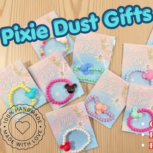 May include: A collection of beaded bracelets on individual display cards featuring the text Pixie Dust Gifts and You've been Pixie dusted. Each bracelet includes a small character-shaped charm in various colors like pink, blue, and yellow.