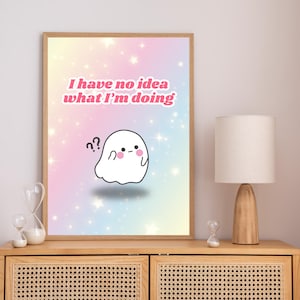 Puede incluir: Impresión artística enmarcada con un simpático fantasma blanco, signos de interrogación y el texto rosa "I have no idea what I'm doing". El fondo es un degradado pastel con estrellas. La obra se exhibe en un mueble de madera.