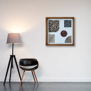 May include: A framed artwork featuring a geometric design made of different coloured pebbles. The artwork is in a wooden frame and is hanging on a white wall.