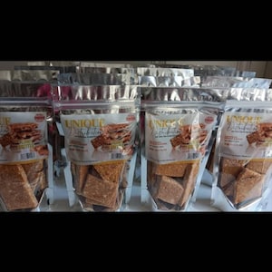 May include: Four resealable bags of peanut brittle snacks labeled "UNIQUE Distribution" with the text "Peanut & Cashew Brittle" and "30g" printed on the front of each bag.