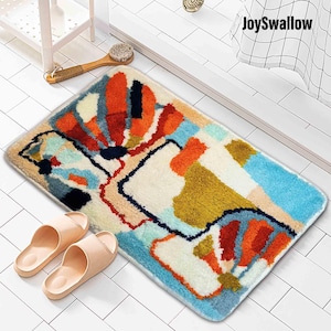 May include: Abstract bath mat with a colorful design featuring shades of blue, orange, red, yellow, and black. The mat is made of a soft, fluffy material.