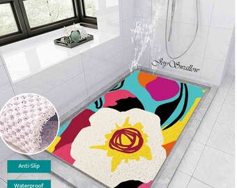 May include: A colourful bath mat featuring a large white flower design against a blue background. The mat is made from a textured material and has a non-slip backing. The text "Joy Swallow" is printed on the mat.