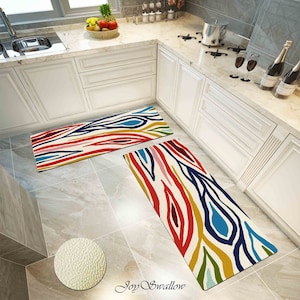 May include: Two colorful kitchen runner rugs with a white background and abstract patterns in red, blue, yellow, green, and pink. The rugs are placed on a tiled floor in a kitchen.