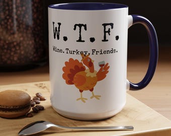 Può includere: Una tazza da caffè in ceramica bianca con bordo e manico blu. La tazza presenta un tacchino dei cartoni animati che tiene un bicchiere di vino e il testo "W.T.F. Wine. Turkey. Friends."