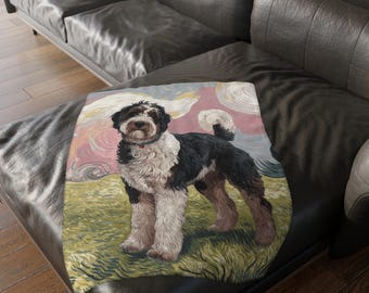 May include: A black and white dog with a fluffy white coat and black markings is depicted in a stylized painting on a throw blanket. The dog is standing on a green grassy field with a pink and blue sky in the background.