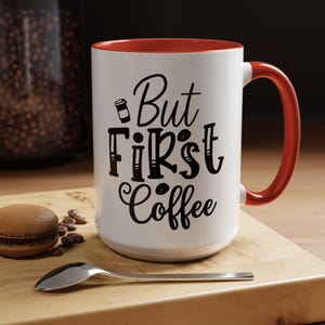 May include: White ceramic coffee mug with a red rim and handle. The mug has black text that reads "But First Coffee" with a small coffee cup icon.