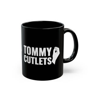 May include: Black ceramic coffee mug with a white graphic that says "TOMMY CUTLETS" and a white fist with the thumb pointing up.