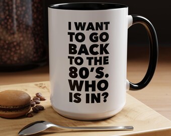 May include: White ceramic mug with a black rim and handle. The mug has black text that reads "I want to go back to the 80's. Who is in?"