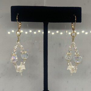 May include: A pair of dangle earrings with white pearl beads, clear crystal beads, and gold accents.