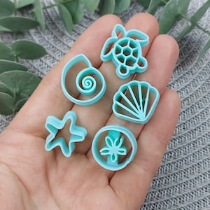 May include: A set of five blue plastic cookie cutters shaped like a seashell, a starfish, a turtle, a sand dollar, and a seashell.