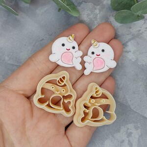 May include: Two white fondant narwhal cookie cutters with gold glitter horns and pink hearts. Two brown plastic narwhal cookie cutters with gold glitter horns and pink hearts.
