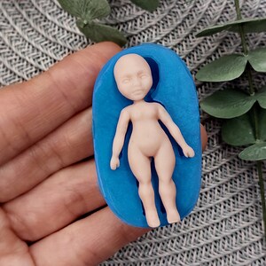 May include: A blue silicone mould for making a small doll figure. The mould is shaped like a person lying on its back with its arms outstretched.