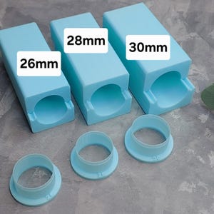 May include: Three light blue cylindrical molds with corresponding circular cutters. The molds are labeled 26mm, 28mm, and 30mm. The cutters are also light blue and have the same size markings.
