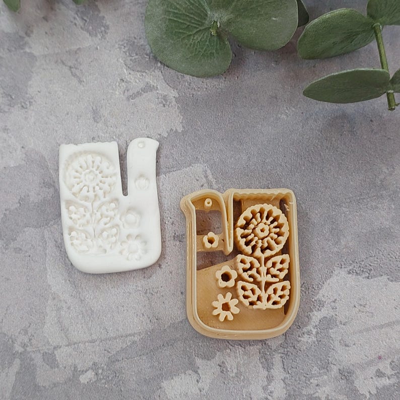 Pu&ograve; includere: Due stampini per biscotti, uno bianco e uno marrone, a forma di fiore stilizzato con foglie. Gli stampini sono in plastica e hanno un design dettagliato.