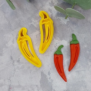 May include: Three plastic chili pepper cookie cutters. Two are yellow and one is red with green accents.