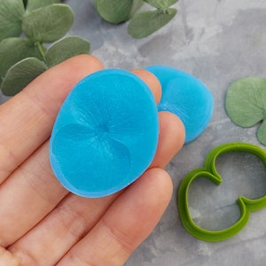 May include: Two blue silicone molds for making polymer clay flowers. The molds are shaped like a flower with five petals.