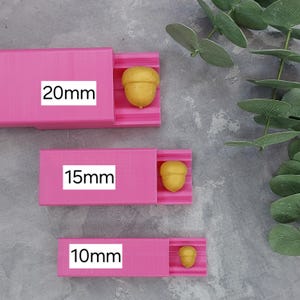 May include: Three pink plastic molds with gold acorn shapes. The molds are labeled 20mm, 15mm, and 10mm.