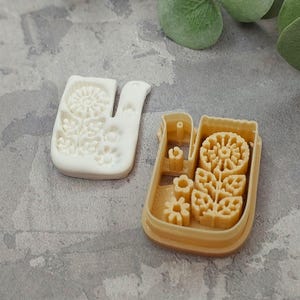 Pu&ograve; includere: Due stampini per biscotti, uno bianco e uno marrone, con un motivo floreale. Lo stampino bianco ha la forma di un uccello e lo stampino marrone ha la forma di un rettangolo.