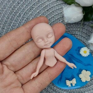 Pode incluir: Um molde de silicone para fazer uma pequena figura de boneca. O molde &eacute; azul e tem um desenho de uma boneca com os bra&ccedil;os estendidos, um la&ccedil;o, uma flor e uma pequena flor.