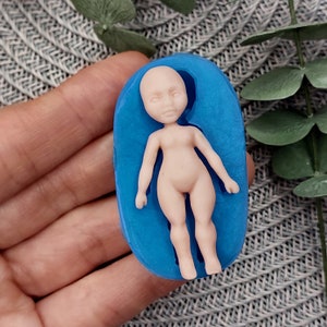 May include: A blue silicone mould for making a small doll figure. The mould is shaped like a person lying on its back with its arms at its sides.