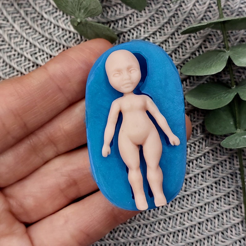 May include: A blue silicone mould for making a small doll figure. The mould is shaped like a person lying on its back with its arms at its sides.