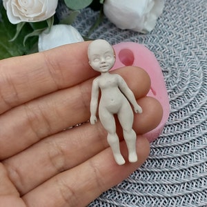 Op de afbeelding: Een klein, ongeverfd, wit poppenfiguurtje met een eenvoudig ontwerp. De pop staat op een roze siliconen mal.