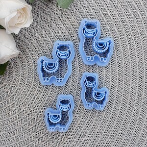 May include: Four blue plastic cookie cutters shaped like llamas. Each llama has a decorative pattern on its chest.