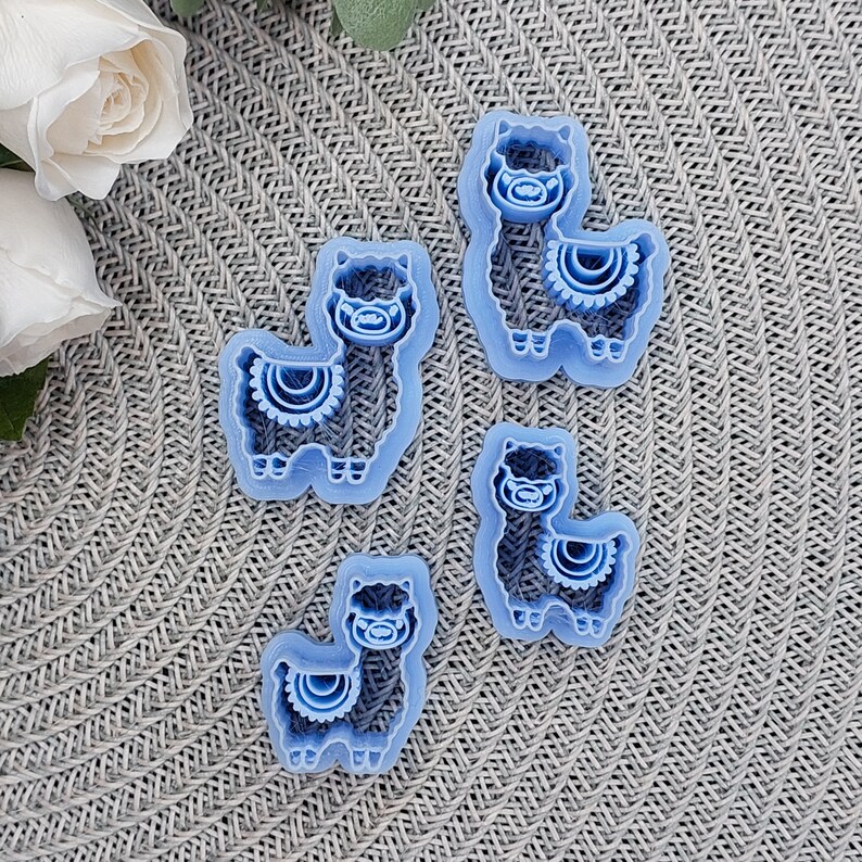 May include: Four blue plastic cookie cutters shaped like llamas. Each llama has a decorative pattern on its chest.