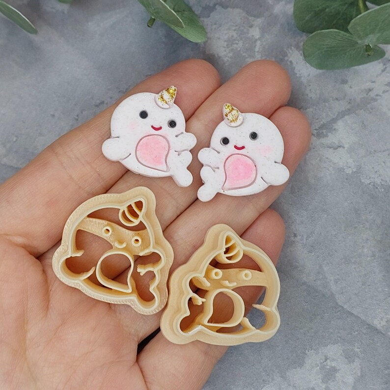 May include: Two white fondant unicorn cookie cutters with gold glitter horns and pink hearts. Two beige plastic cookie cutters shaped like unicorns with gold glitter horns and pink hearts.