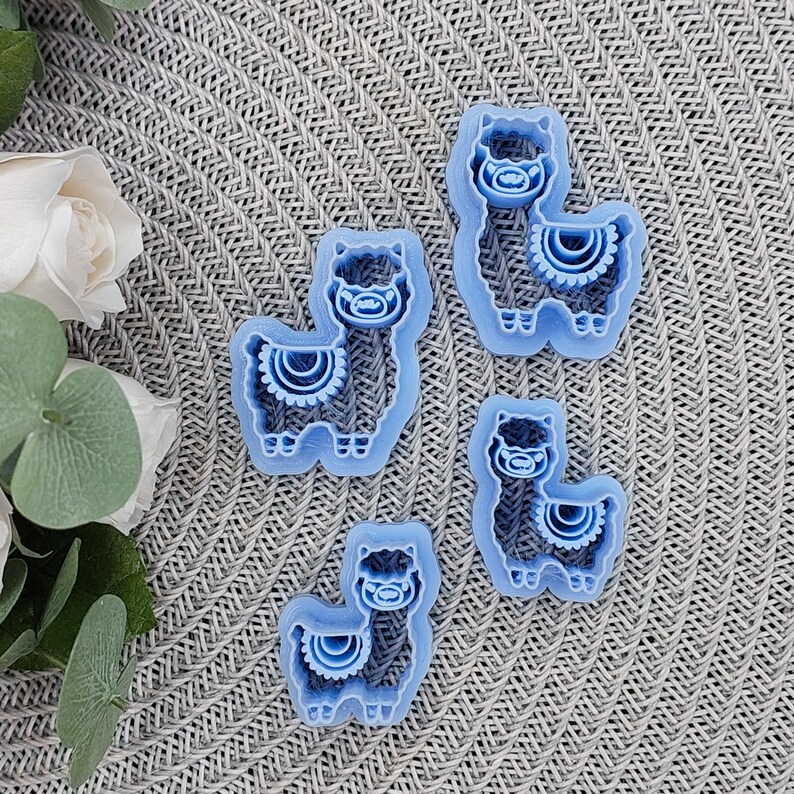 May include: Four blue plastic llama cookie cutters on a gray textured surface. The cookie cutters are different sizes and have a simple design.