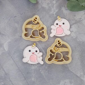 May include: Four cookie cutters shaped like narwhals. Two are plain and two have a striped pattern. The narwhals have a horn, eyes, and a mouth.