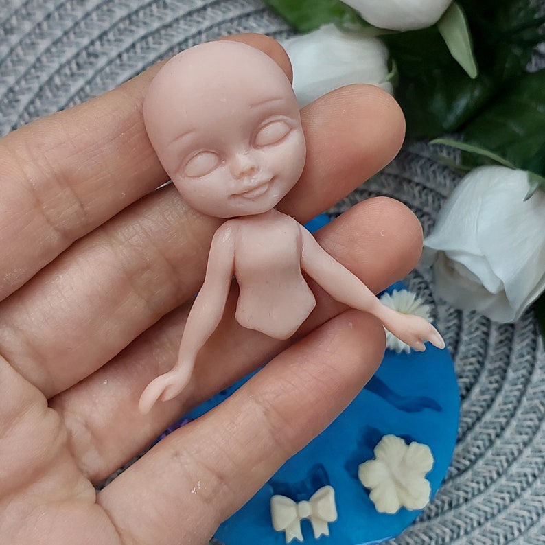 Pode incluir: Uma pequena boneca n&atilde;o pintada feita de argila polim&eacute;rica. A boneca tem um rosto detalhado com os olhos fechados, um nariz pequeno e uma boca ligeiramente aberta. A boneca est&aacute; em pose com os bra&ccedil;os estendidos e as pernas juntas.