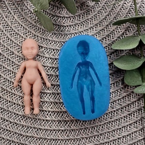 May include: A blue silicone mould for making a doll figure. The mould is shaped like a person with arms outstretched and legs together. A small, nude doll is shown next to the mould.