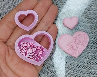 May include: Three pink heart-shaped cookie cutters, one with a simple outline, one with a detailed floral design, and one with a solid heart shape.