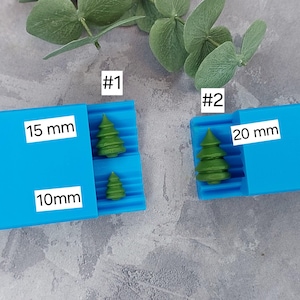 May include: Two blue silicone molds for making Christmas tree ornaments. The mold on the left is labeled #1 and has two cavities, one measuring 10 mm and the other 15 mm. The mold on the right is labeled #2 and has a cavity measuring 20 mm.
