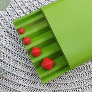May include: A green plastic pill organiser with five compartments. Four red pills are visible in the compartments.