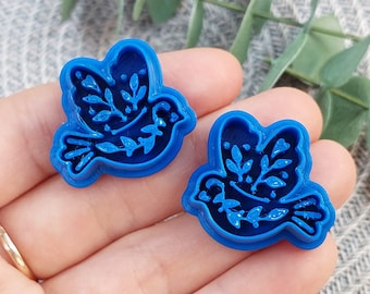 May include: Two blue plastic cookie cutters shaped like a bird with floral designs.