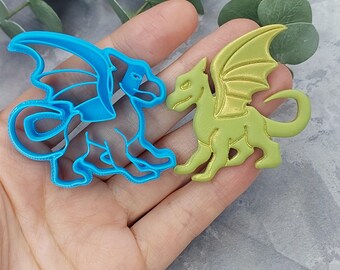 Könnte beinhalten: Zwei Drachen-Ausstecher, einer blau und einer grün. Der blaue Drache ist zusammengerollt mit ausgebreiteten Flügeln. Der grüne Drache steht mit ausgebreiteten Flügeln.