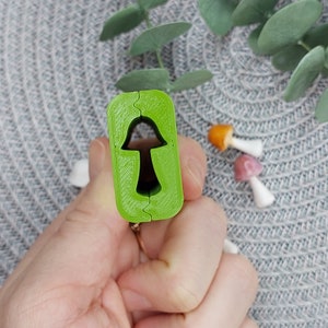 May include: A green plastic mold for making resin mushroom charms. The mold is open and shows the mushroom shape inside.