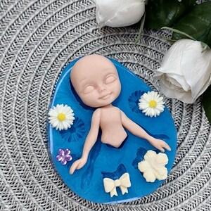 Pode incluir: Um molde de silicone azul com uma cavidade em forma de boneca e v&aacute;rias cavidades em forma de flores e la&ccedil;os. O molde est&aacute; sobre uma superf&iacute;cie cinza texturizada.