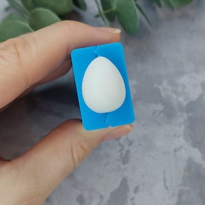 May include: A blue silicone mold for making resin crafts. The mold is shaped like an egg and has a smooth, white surface.
