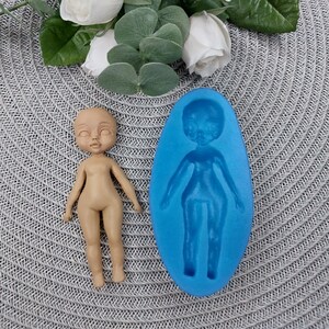 Puede incluir: Un molde de silicona azul para hacer una figura de mu&ntilde;eca. El molde tiene forma de persona con cabeza, brazos, piernas y torso. Se muestra una figura de mu&ntilde;eca terminada junto al molde.