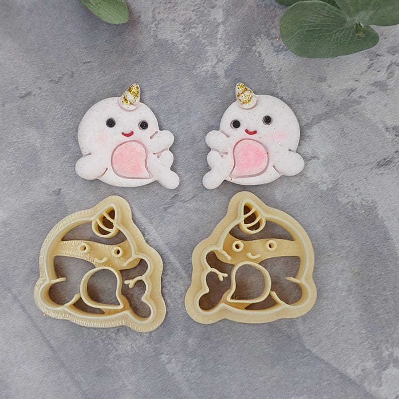 May include: Two white fondant narwhal decorations with gold horns and pink accents, and two matching cookie cutters.