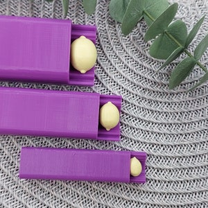 May include: Three purple plastic containers with yellow lemon-shaped objects inside. The containers are stacked on top of each other.