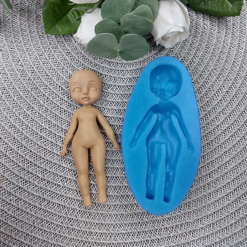 Puede incluir: Un molde de silicona para hacer una figura de mu&ntilde;eca. El molde es azul y tiene la forma de una figura de mu&ntilde;eca. Una figura de mu&ntilde;eca marr&oacute;n est&aacute; al lado del molde.
