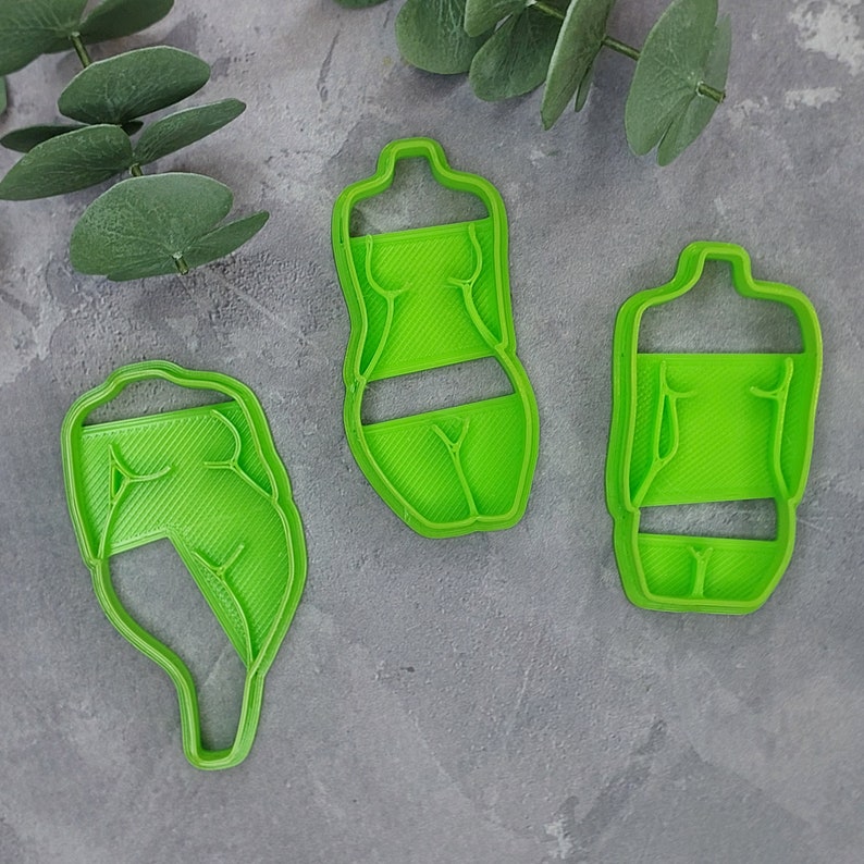 May include: Three bright green cookie cutters in the shape of a torso. The cutters are made of plastic and have a detailed design. The cutters are designed to cut out cookies in the shape of a torso.